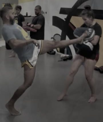 Aluno aplicando chute em aparador durante aula de Muay Thai